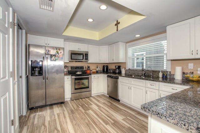 kitchen with white cabinetry, light hardwood / wood-style floors, appliances with stainless steel finishes, and a tray ceiling