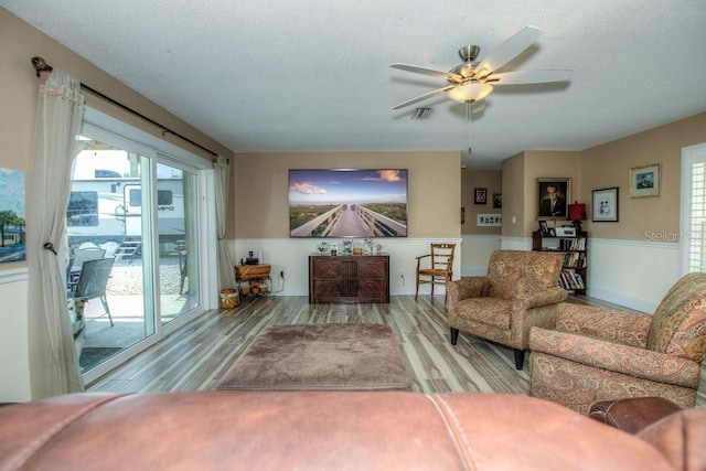 living room featuring light hardwood / wood-style flooring, ceiling fan, and a textured ceiling