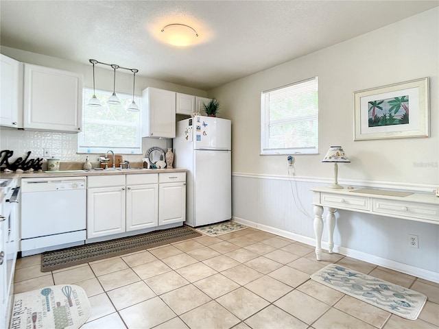 kitchen with plenty of natural light, white appliances, white cabinetry, and light tile floors