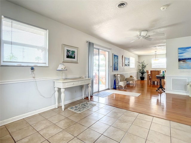 foyer entrance with a textured ceiling, ceiling fan, and light wood-type flooring