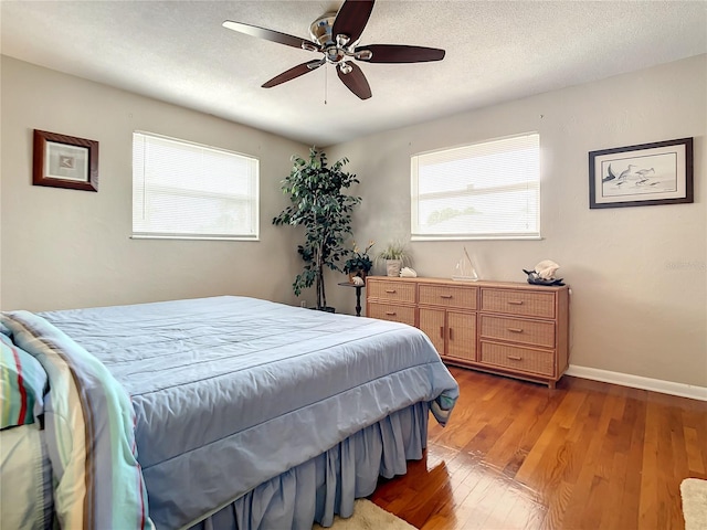 bedroom featuring dark hardwood / wood-style flooring, a textured ceiling, ceiling fan, and multiple windows