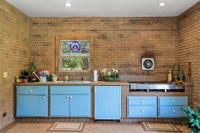 kitchen featuring brick wall, blue cabinetry, and sink