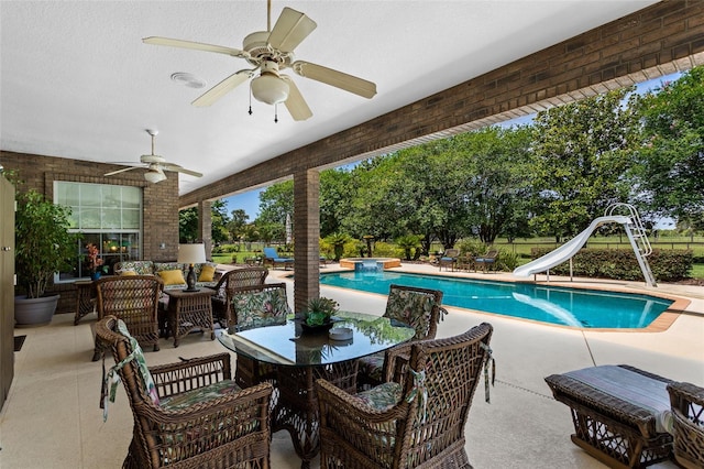 view of swimming pool with outdoor lounge area, a water slide, ceiling fan, and a patio area