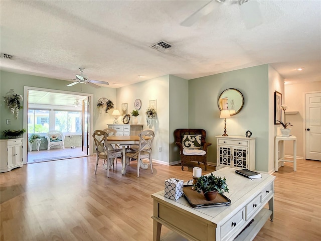 living room featuring light hardwood / wood-style flooring, ceiling fan, and a textured ceiling