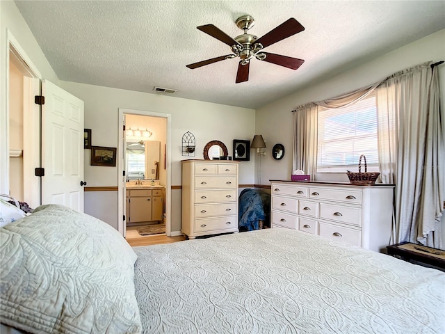 bedroom with ensuite bathroom, light hardwood / wood-style floors, ceiling fan, and a textured ceiling