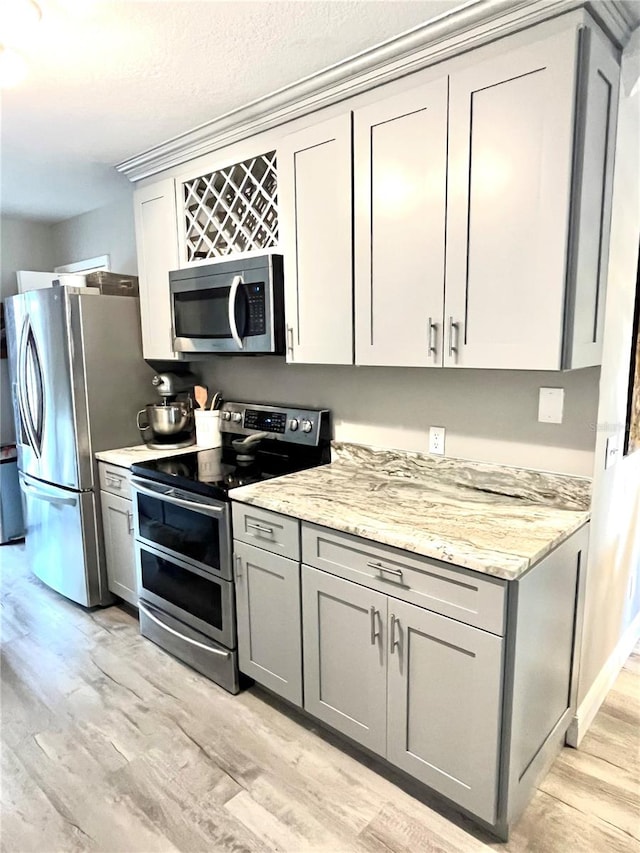 kitchen with light stone countertops, stainless steel appliances, light hardwood / wood-style flooring, and gray cabinets