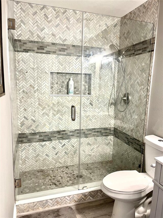 bathroom featuring a shower with door, toilet, and vanity