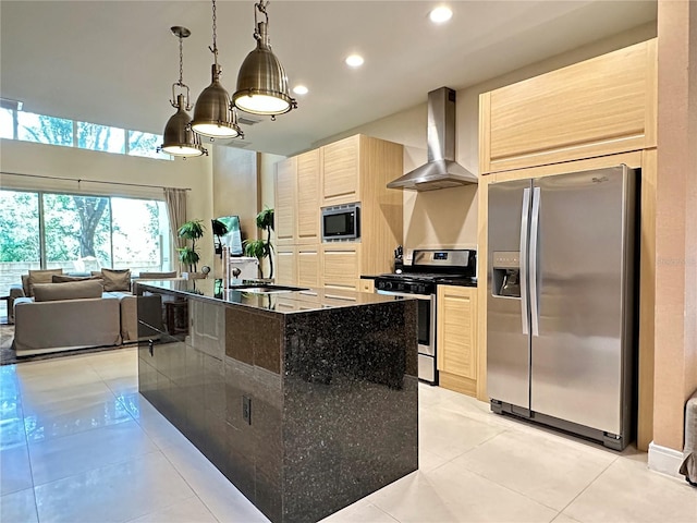 kitchen featuring light brown cabinets, wall chimney range hood, light tile flooring, appliances with stainless steel finishes, and a kitchen island with sink