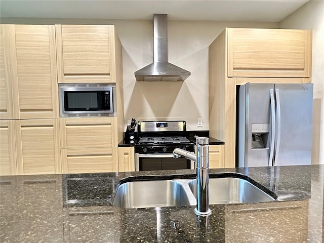 kitchen with wall chimney range hood, light brown cabinetry, appliances with stainless steel finishes, and dark stone countertops