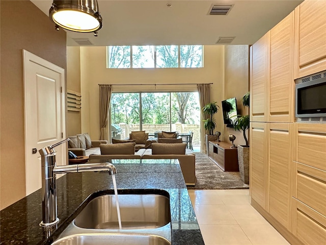 interior space with light brown cabinetry, sink, light tile floors, dark stone counters, and stainless steel microwave