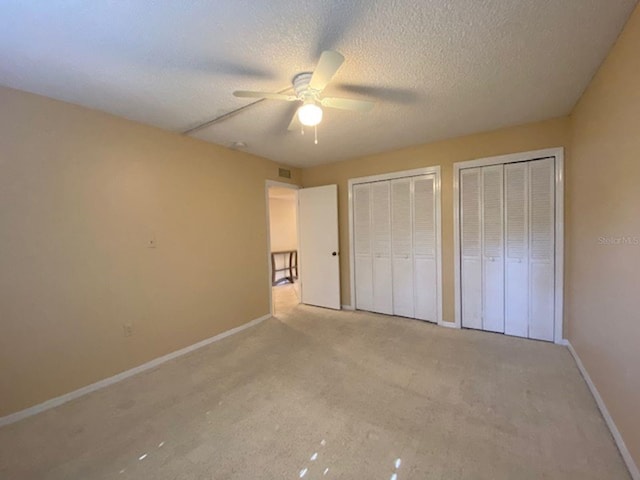 unfurnished bedroom with ceiling fan, a textured ceiling, two closets, and light colored carpet