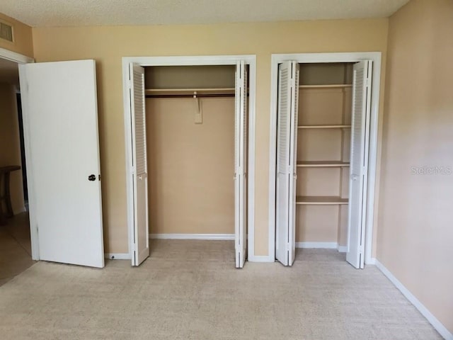 unfurnished bedroom with a textured ceiling, two closets, and light colored carpet