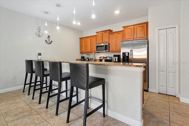 kitchen with light stone countertops, stainless steel appliances, light tile floors, and a breakfast bar