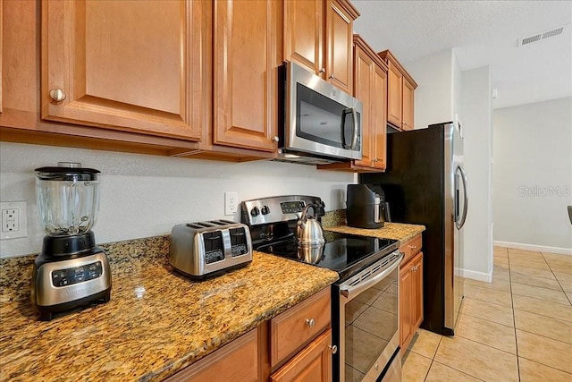 kitchen with light tile flooring, appliances with stainless steel finishes, and light stone counters