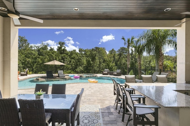 view of swimming pool featuring a bar, ceiling fan, and a patio