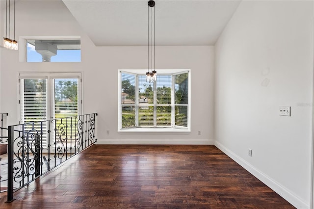 spare room with a notable chandelier, dark hardwood / wood-style floors, french doors, and a wealth of natural light