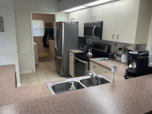 kitchen featuring sink, light tile floors, washer / dryer, stainless steel appliances, and white cabinetry