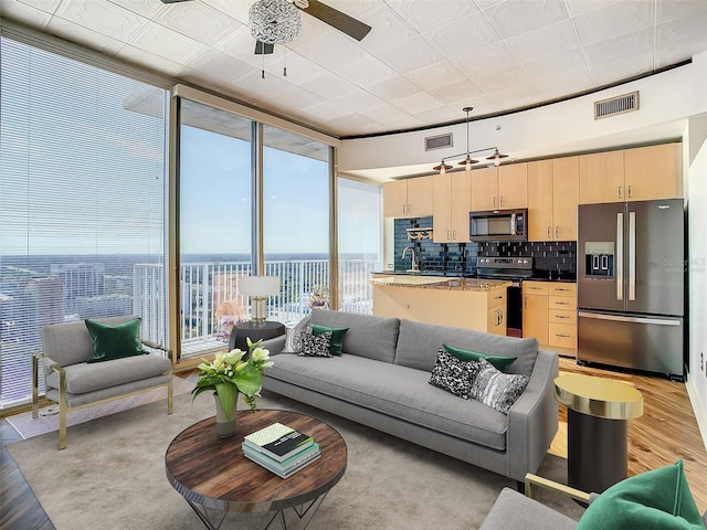 living room featuring light hardwood / wood-style floors, expansive windows, ceiling fan, and a water view