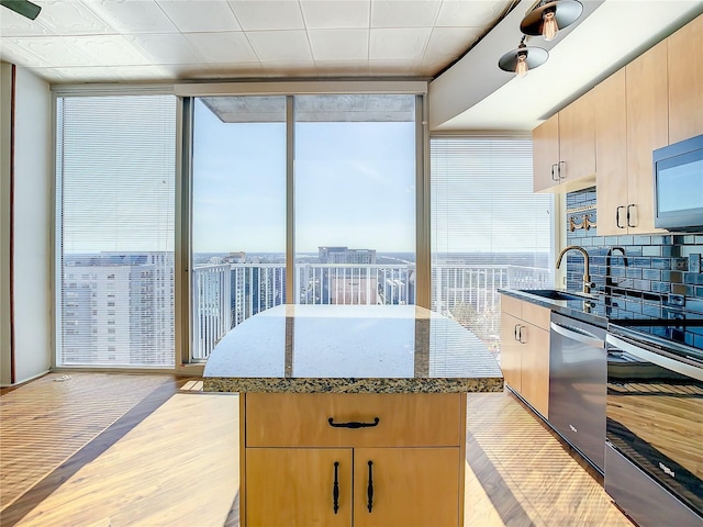 kitchen with sink, a center island, light wood-type flooring, a wall of windows, and stainless steel appliances