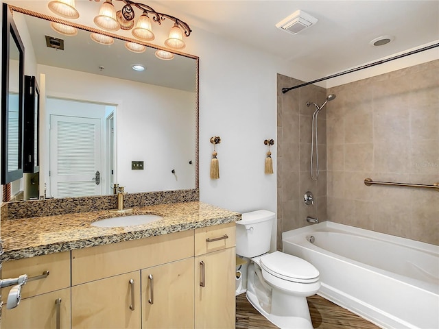 full bathroom with vanity, tiled shower / bath, hardwood / wood-style floors, and toilet