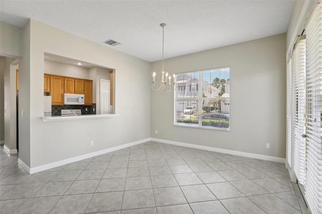 unfurnished dining area featuring light tile patterned floors, a textured ceiling, and an inviting chandelier