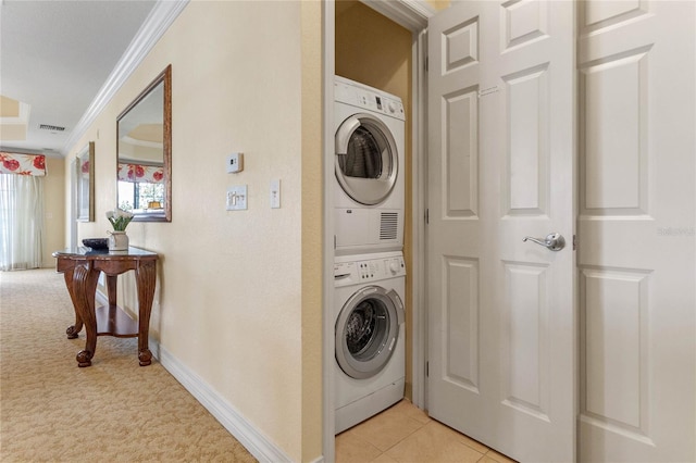 washroom with ornamental molding, stacked washing maching and dryer, and light tile floors