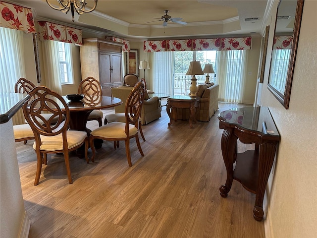 dining area with crown molding, ceiling fan with notable chandelier, a tray ceiling, and hardwood / wood-style flooring