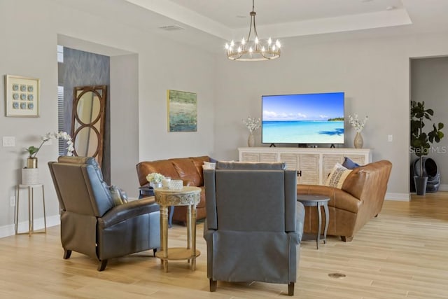 living room with light hardwood / wood-style floors, a tray ceiling, and an inviting chandelier