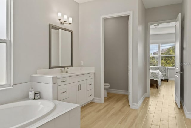 bathroom with hardwood / wood-style flooring, vanity, a relaxing tiled tub, and toilet