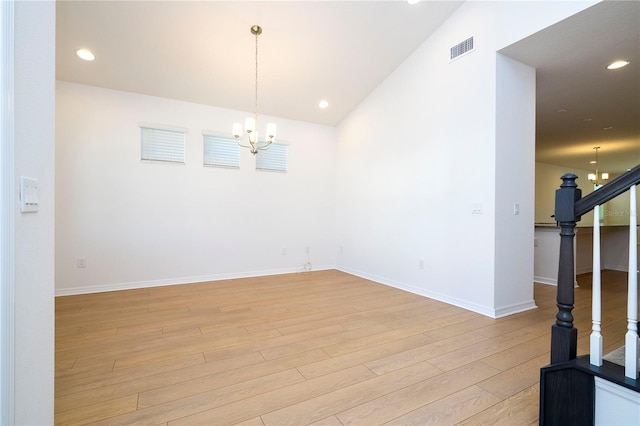 spare room featuring vaulted ceiling, light wood-type flooring, and a notable chandelier