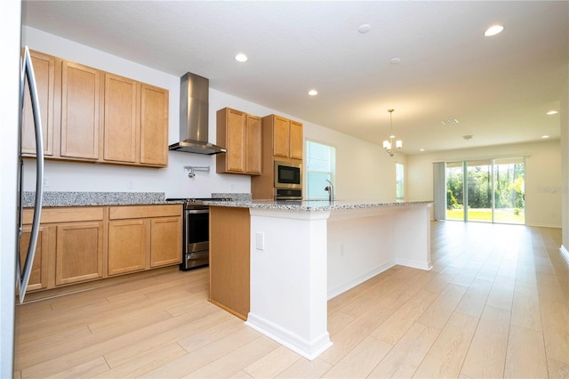 kitchen featuring appliances with stainless steel finishes, wall chimney exhaust hood, hanging light fixtures, an island with sink, and light stone countertops