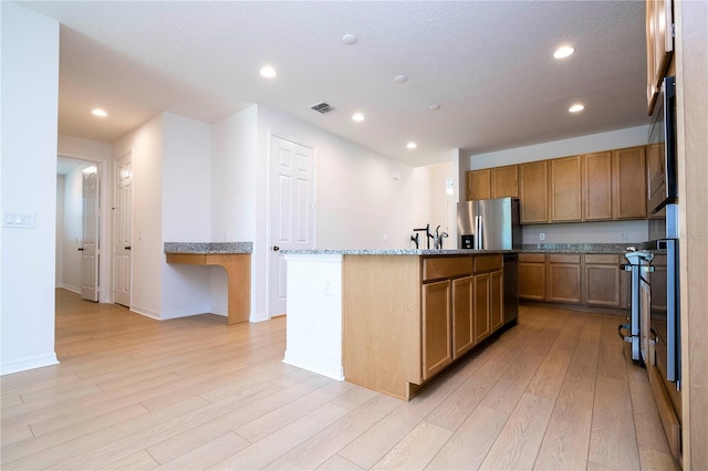 kitchen featuring a kitchen island with sink, light stone countertops, appliances with stainless steel finishes, a breakfast bar area, and light hardwood / wood-style floors