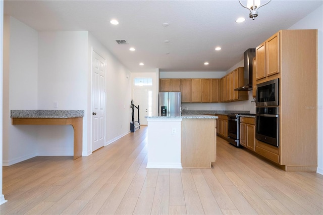 kitchen with light stone counters, wall chimney range hood, light wood-type flooring, stainless steel appliances, and a kitchen island with sink