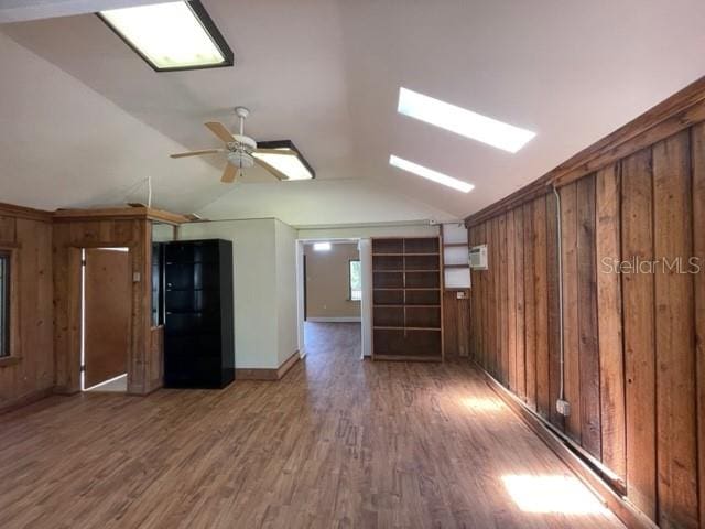 interior space featuring dark hardwood / wood-style floors, lofted ceiling with skylight, ceiling fan, and wooden walls