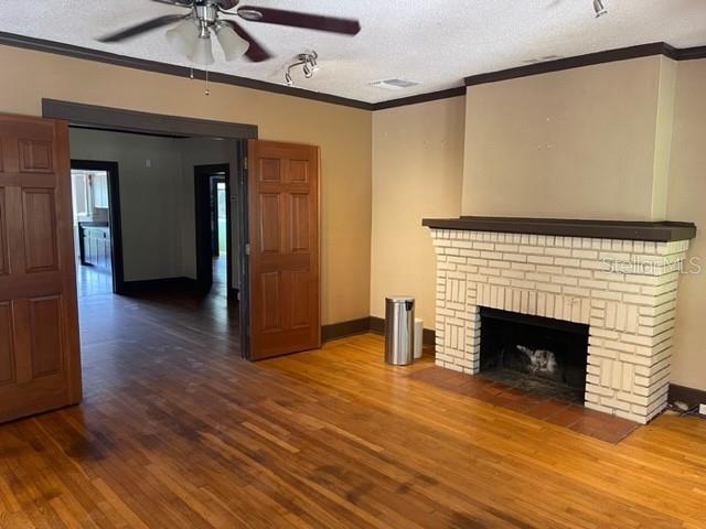 unfurnished living room with crown molding, a fireplace, a textured ceiling, and hardwood / wood-style flooring