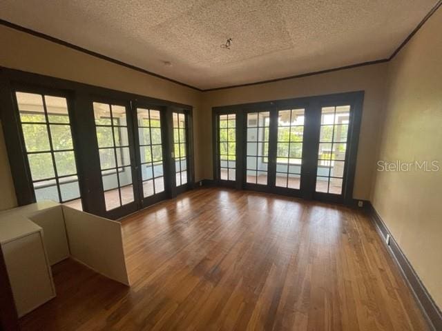 empty room featuring hardwood / wood-style flooring, crown molding, a textured ceiling, and french doors