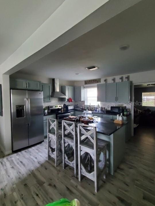 kitchen with wall chimney exhaust hood, appliances with stainless steel finishes, and dark wood-type flooring