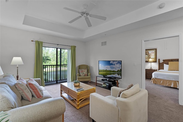 living room featuring ceiling fan, carpet flooring, and a tray ceiling