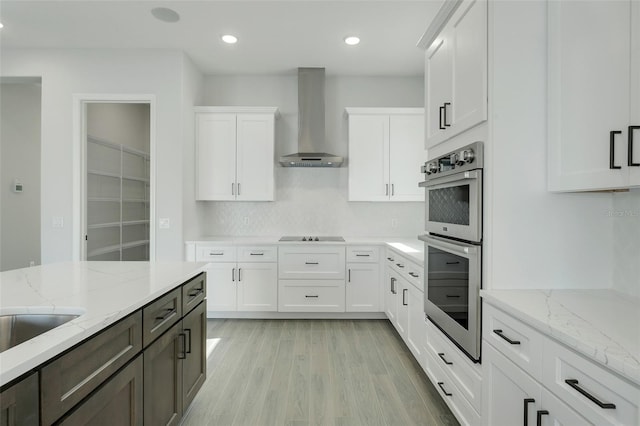 kitchen featuring light stone countertops, wall chimney range hood, stainless steel double oven, and white cabinets