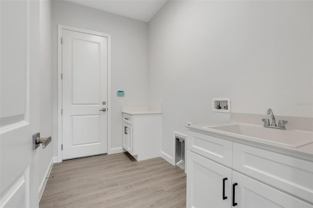 clothes washing area featuring hookup for a washing machine, hookup for an electric dryer, sink, light wood-type flooring, and cabinets