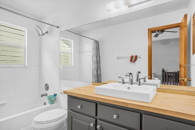 full bathroom featuring toilet, vanity with extensive cabinet space, shower / tub combo with curtain, and ceiling fan