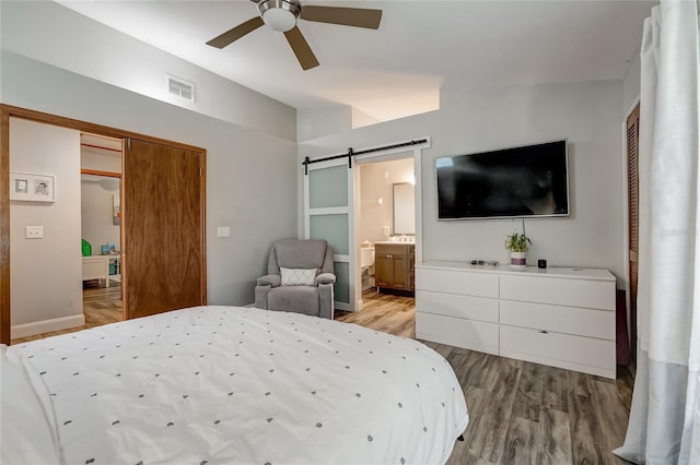 bedroom with a barn door, connected bathroom, ceiling fan, and light wood-type flooring