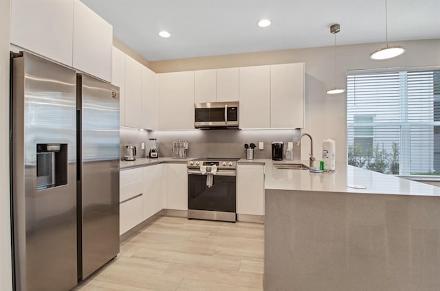 kitchen featuring sink, hanging light fixtures, white cabinets, appliances with stainless steel finishes, and light hardwood / wood-style flooring