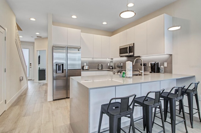 kitchen with light hardwood / wood-style flooring, a breakfast bar area, stainless steel appliances, tasteful backsplash, and white cabinetry