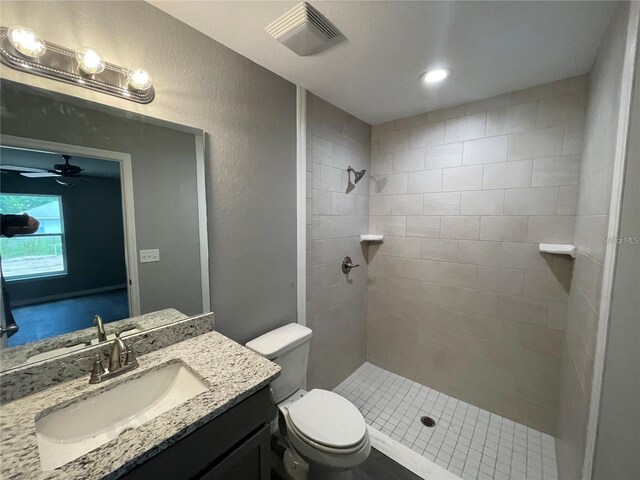 bathroom with vanity, ceiling fan, toilet, and a tile shower