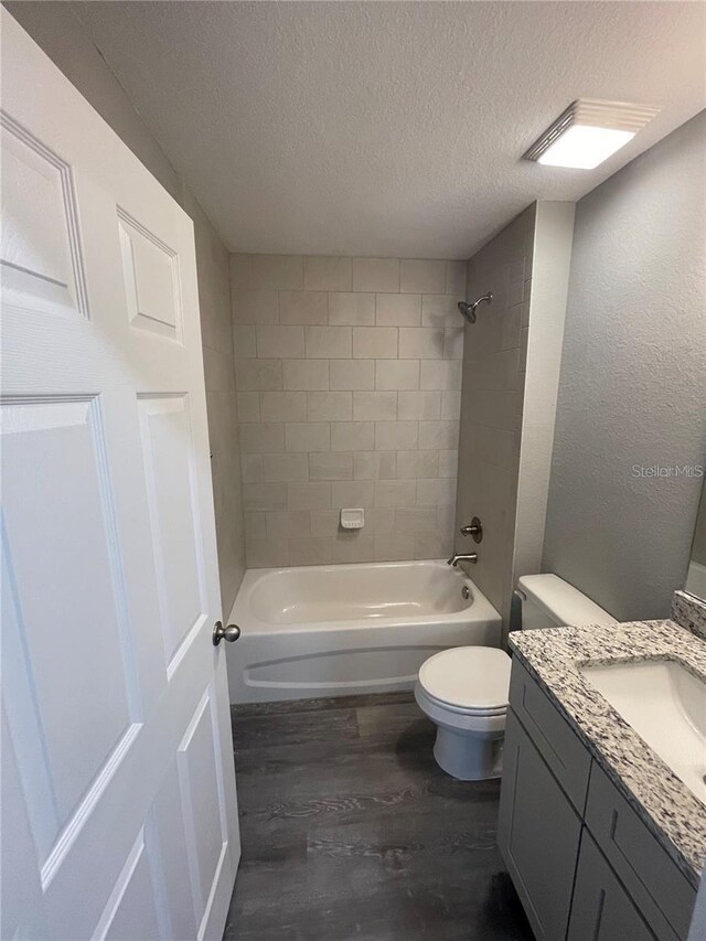 full bathroom featuring hardwood / wood-style flooring, tiled shower / bath combo, vanity, a textured ceiling, and toilet