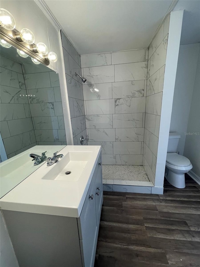 bathroom with tiled shower, oversized vanity, toilet, and wood-type flooring