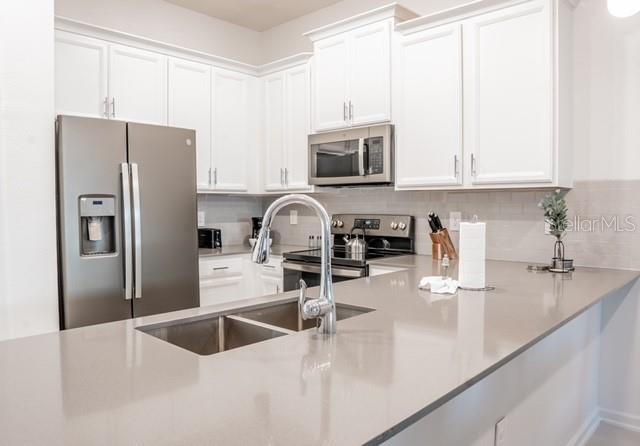 kitchen with white cabinets, backsplash, appliances with stainless steel finishes, and sink