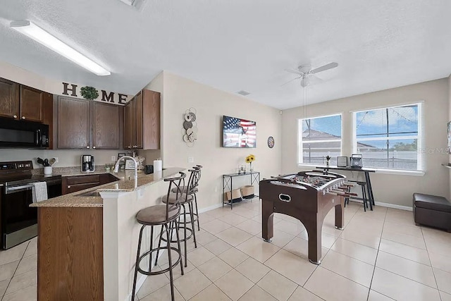 kitchen with kitchen peninsula, light tile patterned floors, sink, and stainless steel range with electric cooktop