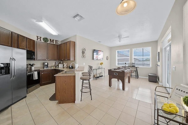 kitchen with light tile patterned floors, kitchen peninsula, a breakfast bar area, stainless steel appliances, and sink